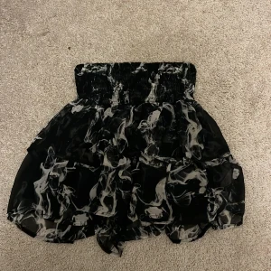 Svartvit volangkjol från KappAhl - Cool svart kortkjol från KappAhl med vitt abstrakt mönster och volanger. Kjolen har bred resår i midjan och är gjord i ett lätt, syntetiskt material som ger ett luftigt intryck. Perfekt för dig som gillar en edgy och trendig stil.