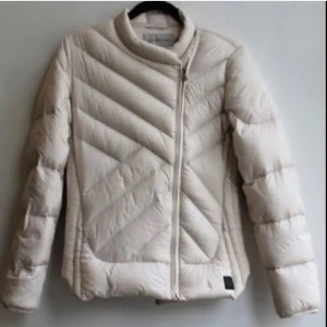 Beige jacka  från Calvin Klein - Snygg beige jacka från Calvin Klein med quiltad design och diskret CK-logga vid nederkanten. Jackan har hög krage, dragkedja och är tillverkad i nylon. Perfekt för kyliga dagar och ger en clean look.