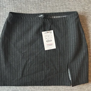 Svart randig kortkjol från Pull&Bear - Snygg svart kortkjol från Pull&Bear med tunna vita ränder och en liten slits framtill. Kjolen har en rak passform och är perfekt för dig som gillar en stilren look. Elastisk midja för extra komfort. Passar till många olika outfits!