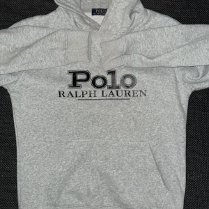 Grå hoodie från Polo Ralph Lauren - Säljer en grå hoodie från Polo Ralph Lauren med stor logga framtill. Klassisk känguruficka, huva med dragsko och mjukt material. Perfekt för chill dagar eller när du vill ha en clean streetstyle-look.