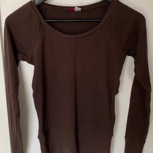 Brun långärmad tröja från H&M - En enkel och stilren brun långärmad tröja från H&M. Tröjan har rund halsringning och ribbad nederkant samt ärmar. Tillverkad i mjuk bomull som är skön mot huden. Perfekt att matcha med jeans eller kjol för en chill look.