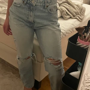 Ljusa ripped jeans från Zara - Säljer ett par ljusblå jeans från Zara i storlek 34. Modellen är högmidjad med raka ben och slitna detaljer vid knäna för en trendig, avslappnad look. Klassisk femficksdesign och tillverkade i bomull. Perfekta för dig som gillar streetstyle. Byxornas längd är 96 cm. 