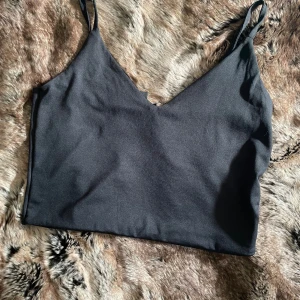 Svart linnetopp med smala axelband - Svart crop top med smala axelband och mjuk, slät yta. v-ringad