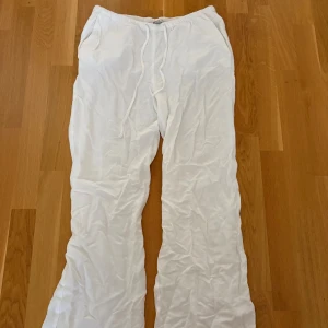 Vita linnebyxor med snörning - Säljer ett par vita linnebyxor med avslappnad passform och resår i midjan samt snörning. Byxorna har raka ben och sidofickor, perfekta för varma dagar och en chill stil.