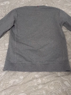 Grå sweatshirt från Les Deux - Säljer en stilren grå sweatshirt från Les Deux med broderad logga på bröstet. Tröjan har rund hals, ribbade muddar vid ärmslut och nederkant samt är tillverkad i 100% bomull. Perfekt för chill dagar och enkel att matcha med jeans eller joggers.