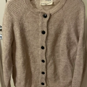 Beige kofta i 49 % ull från Selected Femme, S/M - Mysig beige kofta från Selected Femme med rund halsringning och knappar framtill. Koftan är finstickad/ribbstickad och har långa ärmar. Materialmix med ull, polyester och nylon för extra komfort. Perfekt till lager på lager under kyliga dagar. Jättefint skick ✨ enda defekten är att översta knapphålet har slits pga knappen har gnagt emot och det har gjort stickningen tunn runt knapphålet, syns främst när tröjan är uppknäppt. Därav sätter jag ett lägre pris. 