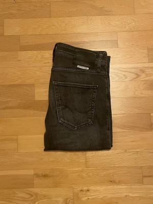 Jack & Jones Regular Clark jeans grå - Snygga grå jeans från Jack & Jones, modell Regular Clark. Klassisk femficksdesign med raka ben och normal passform. Jeansen har metallknappar och detaljerade sömmar. Perfekt för dig som gillar stilrena och bekväma jeans.