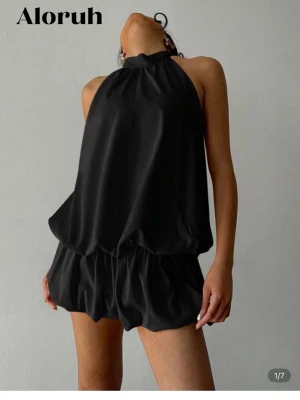 Svart klänning i satin-look - Snygg svart klänning från Aloruh med halterneck och öppen rygg. Klänning  har en lös och luftig passform med ballongliknande shorts och knytning i nacken. Materialet har en satinliknande glans som ger en lyxig känsla. Perfekt till nyår❤️