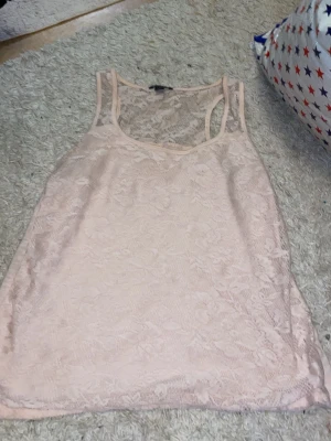 Beige spetslinne från Amisu - Säljer ett ljusbeige linne från Amisu i storlek L. Linnet har ett vackert spetsmönster över hela plagget och är ärmlöst med smala axelband. Perfekt för sommarens varma dagar eller när du vill ha en romantisk touch på din outfit.