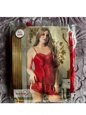 Röd satinväst med spetsdetalj - Snygg röd väst i satin från Matilda Secret med tunna axelband och spetsdetalj upptill. Västen har en glansig finish och en feminin look som passar perfekt för dig som gillar att sticka ut.