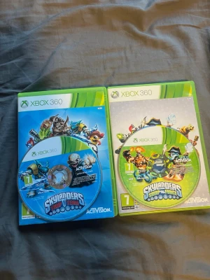 Skylanders Trap Team & Skylanders Swap Force Xbox 360 - Två Skylanders-spel till Xbox 360: Trap Team och Swap Force. Båda med originalfodral och skivor i fint skick, inga synliga repor eller skador. Perfekt för samlare eller familjer som vill ha rolig spelunderhållning.