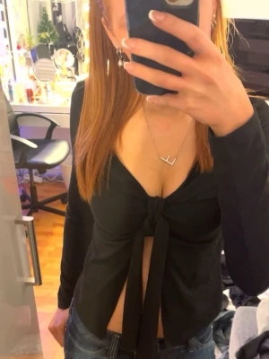Svart långärmad omlottopp med knyt - Säljer en svart långärmad topp med snygg omlottdesign och knyt framtill. Toppen har djup v-ringning och är croppad så magen syns. Materialet är mjukt och stretchigt, perfekt att styla med jeans eller kjol.