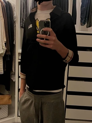 Svart Burberry skjorta med rutig detalj (PRISET ÄR FAST, EJ PRUTBART) - Svart skjorta från Burberry med klassisk rutig beige och röd insida på krage och manschetter. Långärmad modell med vit broderad logga på bröstet. Snygg och stilren, perfekt för dig som gillar ikoniska detaljer och cool design.