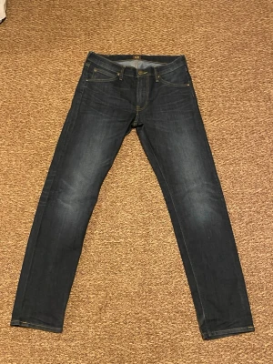 Mörkblå skinny jeans från Lee - Snygga mörkblå jeans från Lee med klassisk femficksdesign och gul kontrastsöm. Modellen är skinny med smal passform och raka ben. Jeansen har en läderpatch med Lee-logga bak i midjan och är tillverkade i slitstarkt denimtyg.
