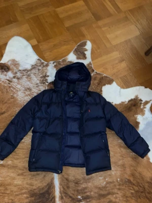 Blå puffer jacka från Ralph lauren  - Säljer den här varma, snygga, sköna, blåa jackan från Ralph Lauren, perfekt för vintern, i storlek XL (barnstorlek). Passar XS-S i vuxenstorlek, men snarare XS.  Jackan har inga defekter överhuvudtaget och köptes för 3300 kr nypris.