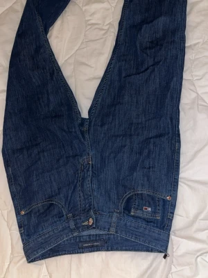 Tommy Hilfiger blå jeans straight fit - Snygga blå jeans från Tommy Hilfiger med klassisk straight fit och normal passform. Jeansen har tydliga sömmar, fem fickor och ett litet Hilfiger-märke på fickan. Materialet är jeans i bomull och färgen är mörkblå. Perfekt för dig som gillar stilrena och tidlösa jeans.