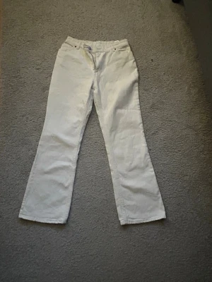 Vita bootcut jeans - Säljer ett par vita jeans med bootcut-snitt. Byxorna har klassisk femficksdesign och är tillverkade i ett mjukt jeanstyg. Passformen är normal och midjan är midwaist. 