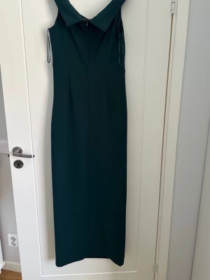 Mörkgrön långklänning från Bubbleroom - Snygg mörkgrön långklänning från Bubbleroom Occasion i storlek 40. Klänningen har omlott-detalj vid halsen och är ärmlös med en elegant, figurnära passform. Tillverkad i mjuk polyester med lite stretch för extra komfort.
