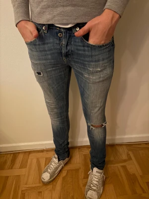Dondup George Jeans - Säljer ett par Dondup George jeans i blå tvätt med slitningar och hål vid knäet. Modellen är skinny med låg midja och klassiska fem fickor. Jeansen har orangea sömmar och är gjorda i stretchig bomull för skön passform.