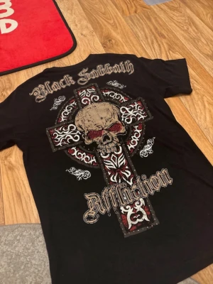 Affliction X Black sabbath t shirt  - GRAILLLL hella fire, bought in the early 2000s but still has 9/10 condition 100% of the rhinestones are still intact if not 99%. Hella good taken care of🙏 Only defect is the small cuts on the neck and little on the end of the sleeves! Nothing noticable