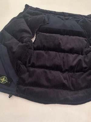 Stone Island mörkblå dunväst i manchester - Säljer en riktigt snygg mörkblå dunväst från Stone Island med breda manchesterpaneler och två stora fickor framtill. Västen har dragkedja och klassisk Stone Island-logga på ena fickan. Perfekt för lager-på-lager och streetwear.