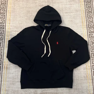 Polo ralph lauren hoodie - Säljer du min polo ralph lauren hoodie i svart med en röd detalj den är i nyskick och aldrig använd samt inga defekter skulle säga att den passar runt 180 med några centimeter marginal