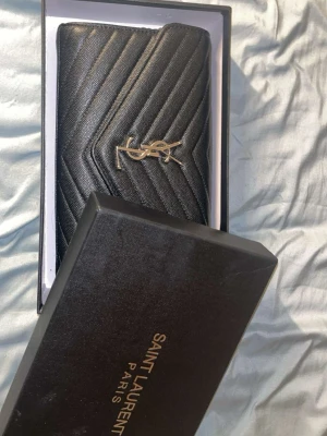 Svart väska YSL - Säljer en svart kuvertväska från Saint Laurent med YSL-logga i guld på framsidan. Väskan är nästan helt ny och har i princip inte används. Den är äkta. Låda medföljer. Börjar priset på 6500kr. Går att diskutera.