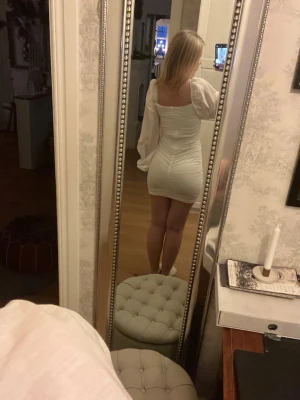 Vit klänning med puffärmar - Supersöt vit kort klänning med långa puffärmar och rynkade detaljer från Nelly. Den har en fyrkantig urringning och sitter tight över kroppen för en snygg siluett. Använd 1 gång! Storlek XS men funkar helt okej på mig som vanligtvis har S. 