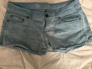 Ljusblå jeansshorts från Bershka - Säljer ett par ljusblå jeansshorts från Bershka i storlek 38. De har klassisk femficksdesign, låg midja och råa kanter nedtill för en chill vibe. Materialet är mjuk bomull och de stängs med knapp och dragkedja. Perfekta för varma dagar!