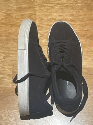 Svarta sneakers från vagabond  - Säljer ett par stilrena svarta sneakers från vagabond med vit sula och klassisk snörning. Ovandelen är i mocka och de har en rund tå samt platt sula. Perfekta för dig som gillar enkel och clean stil.