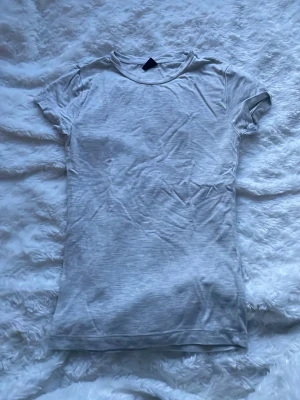 Ljusgrå basic t-shirt - En enkel ljusgrå t-shirt med rund hals och korta ärmar. Tillverkad i mjukt bomullstyg som känns skönt mot huden. Perfekt att matcha med jeans eller shorts för en clean och avslappnad look.