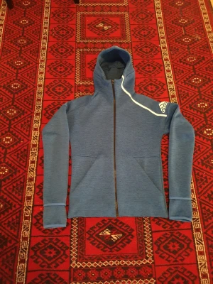 Addidasjacka med snygg design och perfekt passform - Addidasjacka i perfekt skick. Snygg färg som går ihop med nästan alla andra färger. Smart material. Andas bra i alla väder. Lättvikt och torkar lätt, både när man vill vara välklädd eller träna. Står även emot och håller torrt på insidan vid fuktigt väder  Ny pris 1700. Storlek XS men passar även en person med storlek smal. 