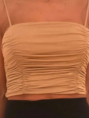 Beige croppad linnetopp med rynk - Trendig beige croppad linnetopp med smala axelband och snygga rynkade detaljer längs sidorna. Perfekt för varma dagar och enkel att matcha med både jeans och kjol. Mjuk och stretchig känsla.