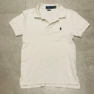 Ralph lauren pike - Klassisk vit pikétröja från Polo Ralph Lauren i slim fit-modell. Tröjan har korta ärmar, krage med knappar och den ikoniska broderade loggan på bröstet. Tillverkad i mjuk bomull som känns skön mot huden.