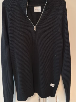 Svart ribbad stickad tröja Jack & Jones - Säljer en svart ribbad stickad tröja från Jack & Jones i storlek S. Tröjan har hög krage och en snygg half zip-dragkedja framtill. Perfekt för dig som gillar en enkel men stilren look med långärmad passform. Kan även passa i M
