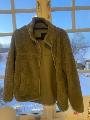 Beige teddyjacka från 157 - Mysig beige teddyjacka från 157 i storlek S. Jackan har hög krage, dragkedja framtill och två sidofickor. Perfekt för kalla dagar när du vill vara både varm och snygg. Materialet är fluffigt och ger en riktigt chill vibe.
