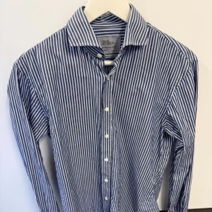 Randig skjorta från Oscar Jacobson - Snygg blå och vit randig skjorta från Oscar Jacobson. Klassisk krage, långa ärmar och vita knappar framtill. Tillverkad i mjuk bomull med exklusiv känsla och stilren look. Perfekt för dig som gillar tidlös design och vill ha något som alltid funkar.