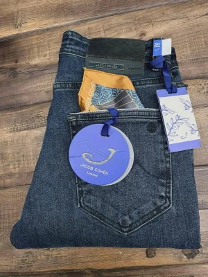 Jacob Cohën mörkblå jeans limited - Snygga mörkblå jeans från Jacob Cohën Limited med klassisk femficksdesign och exklusiva detaljer som färgglad näsduk i fickan och märkestaggar. Jeansen har raka ben och är tillverkade i mjukt jeansmaterial med diskreta kontrastsömmar.