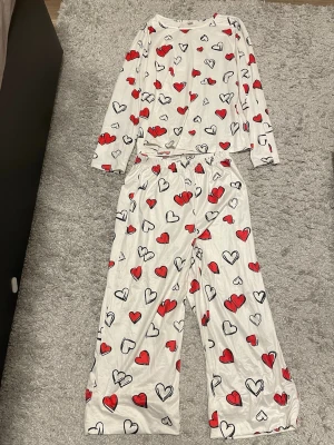 Söt pyjamas med hjärtan – supermysig & bekväm - Superfin pyjamas i vitt med röda och svarta hjärtan – perfekt för mysiga kvällar och lata morgnar ❤️🧸  Består av långärmad tröja och matchande byxor. Mjuk och skön mot huden, sitter bekvämt och känns lätt att ha på sig.   Har bara använt den en gång så den är i mycket fint skick. Passar perfekt nu när man bara vill chilla hemma, kolla serie eller sova extra gott 😴🫶 Enkel men ändå gullig🥹riktig feel good-pyjamas. Den är från barnavdelningen på SHEIN som man kan se på bild 2 och 3.