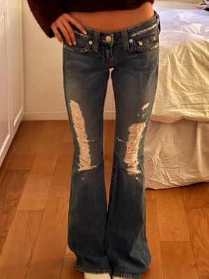 True religion vintage jeans med slitningar - Säljer ett par blå bootcut jeans med kraftiga slitningar på framsidan av benen. Jeansen har väldigt låg midja. Säljer dem pågrund av att dem är lite för stora för mig men dem är verkligen så otroligt snygga. Köpta second hand och jag själv har inte använt dem sen jag fick dem. Har inte upptäckt några defekter från förra ägaren. Storlek 25!
