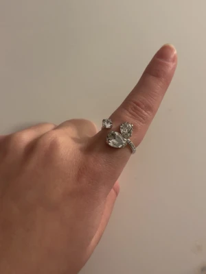 Caroline Svedbom silverring med stenar - Säljer en snygg silverfärgad ring från Caroline Svedbom med tre stora, glittrande stenar i olika former. Ringen har en öppen design och kommer i originalask och påse. Perfekt för dig som gillar statement-smycken! Ringen är helt oanvänd