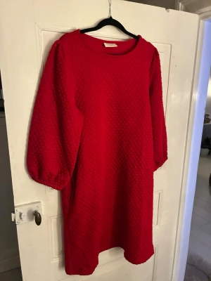 Röd strukturerad klänning från Freequent - Röd klänning från Freequent i storlek XX-Large. Den är dock liten i storlek så passar snarare L/XL. Klänningen har en cool strukturerad yta, trekvartsärmar med resår och praktiska fickor i sidorna. Rak passform och rund halsringning. Perfekt för dig som gillar färg och vill sticka ut.