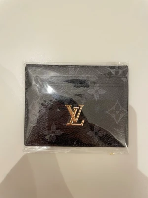 L och V svart plånbok - Snygg svart plånbok med klassiskt monogrammönster och guldfärgad L och V logga framtill. Tillverkad med flera fack för kort. Perfekt accessoar för dig som gillar lyxiga detaljer och stilren design.