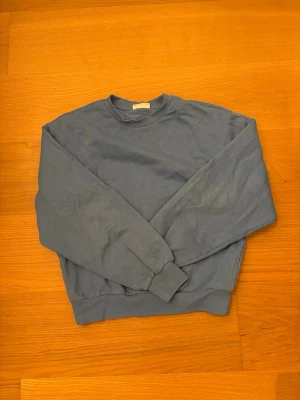 Blå sweatshirt från Gina Tricot XS - En basic blå sweatshirt från Gina Tricot i modellen Basically Basics. Tröjan har rund hals, ribbade muddar vid ärmslut och midja samt lång ärm. Perfekt för en chill och avslappnad stil. 70% bomull, 30% Polyester.
