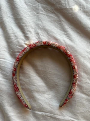 Blommigt diadem - Säljer ett fluffigt hårband med blommigt mönster i rosa, rött och vitt. Hårbandet är vadderat och har en mjuk, rundad form som ger en söt och trendig look. Perfekt accessoar för att piffa upp frisyren. Aldrig använd 
