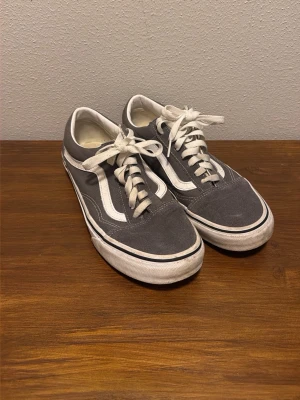 Gråa Vans Old Skool sneakers - Säljer ett par klassiska Vans Old Skool sneakers i grått med vita detaljer. Skorna har den ikoniska sidostripen, snörning och låg profil. Ovandelen är tyg för en skön och stilren look.