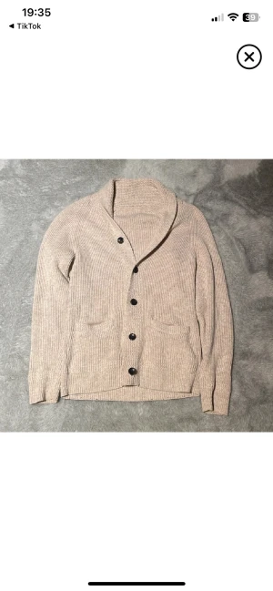 Beige ribbad kofta med stora knappar - Riktigt snygg beige kofta med ribbad struktur och svarta knappar💪. Koftan har två fickor och en bred krage. Nyskick 🙌 passar S/M.