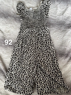 Leopardmönstrad byxdress i storlek 92 - Säljer en söt byxdress med leopardmönster i svart och vitt. Byxdressen har puffärmar, smock upptill och vida ben. Perfekt för dig som gillar djurmönstrat och vill ha något bekvämt men ändå trendigt.🌸 Fint använt skick. Storlek 92