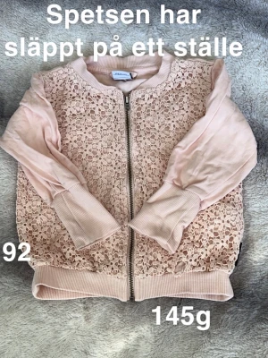 Ljusrosa spetskofta med dragkedja - Supersöt ljusrosa kofta från Polarn o pyret med spets framtill och mjuka ribbade muddar. Koftan har dragkedja och långa ärmar, perfekt för lager på lager under vår och sommar. Spetsdetaljerna ger ett romantiskt intryck.🌸 Finns en fläck och spetsen har släppt på ett ställe. Storlek 92