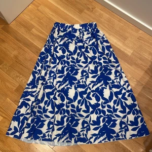 Blåvit långkjol med bladmönster - Säljer en långkjol med elastisk midja och snyggt blått bladmönster på vit botten. Kjolen har en luftig känsla och passar perfekt till varma dagar. Materialet känns mjukt.